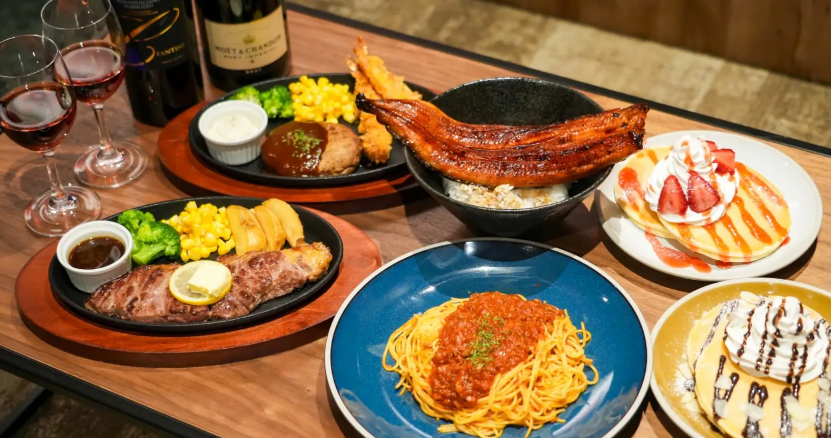 パスタ、ステーキ、うな丼、デザート、ワインなどが並べられたテーブルの写真